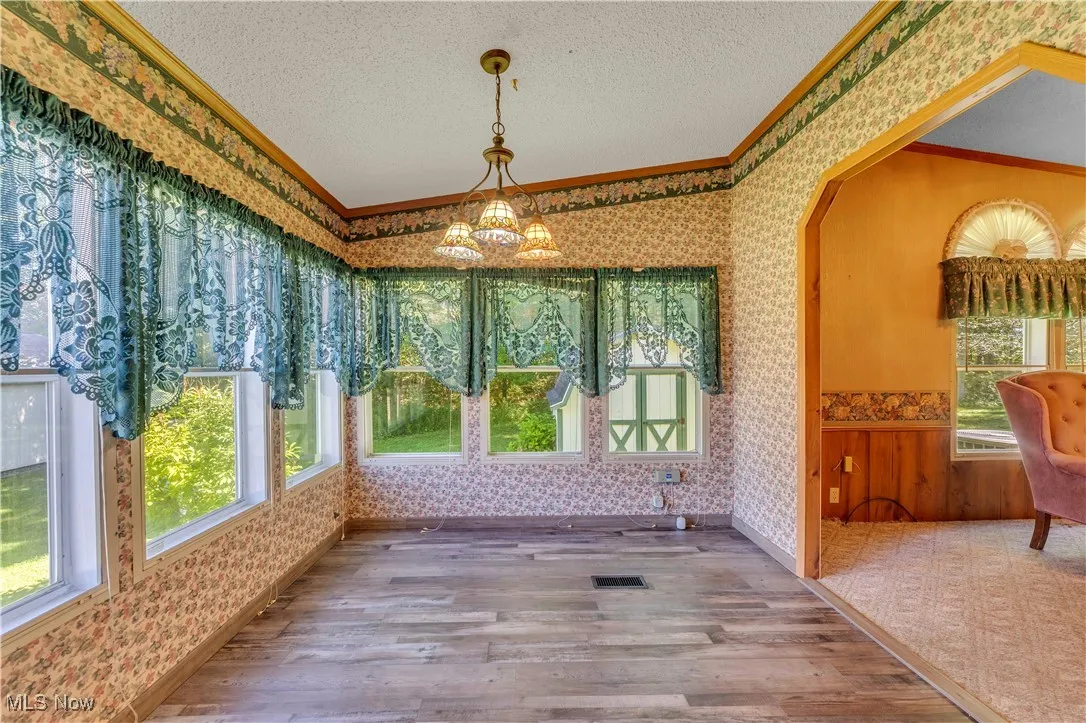 Unfurnished sunroom featuring wallpapered walls, wood finished floors, crown molding, a textured ceiling, and a chandelier