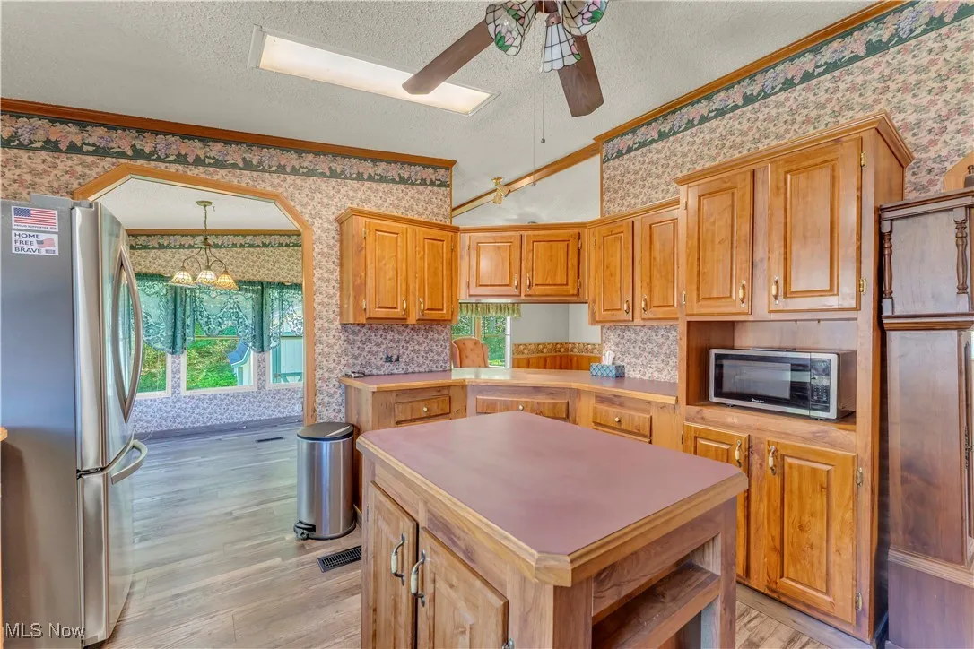Kitchen with appliances with stainless steel finishes, a center island, light countertops, light wood-style floors, and a textured ceiling