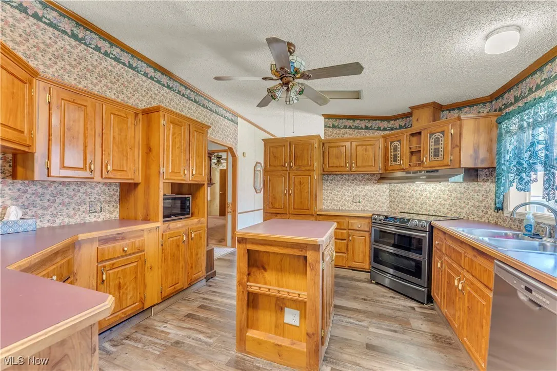 Kitchen with open shelves, stainless steel appliances, light countertops, light wood-style floors, and a textured ceiling