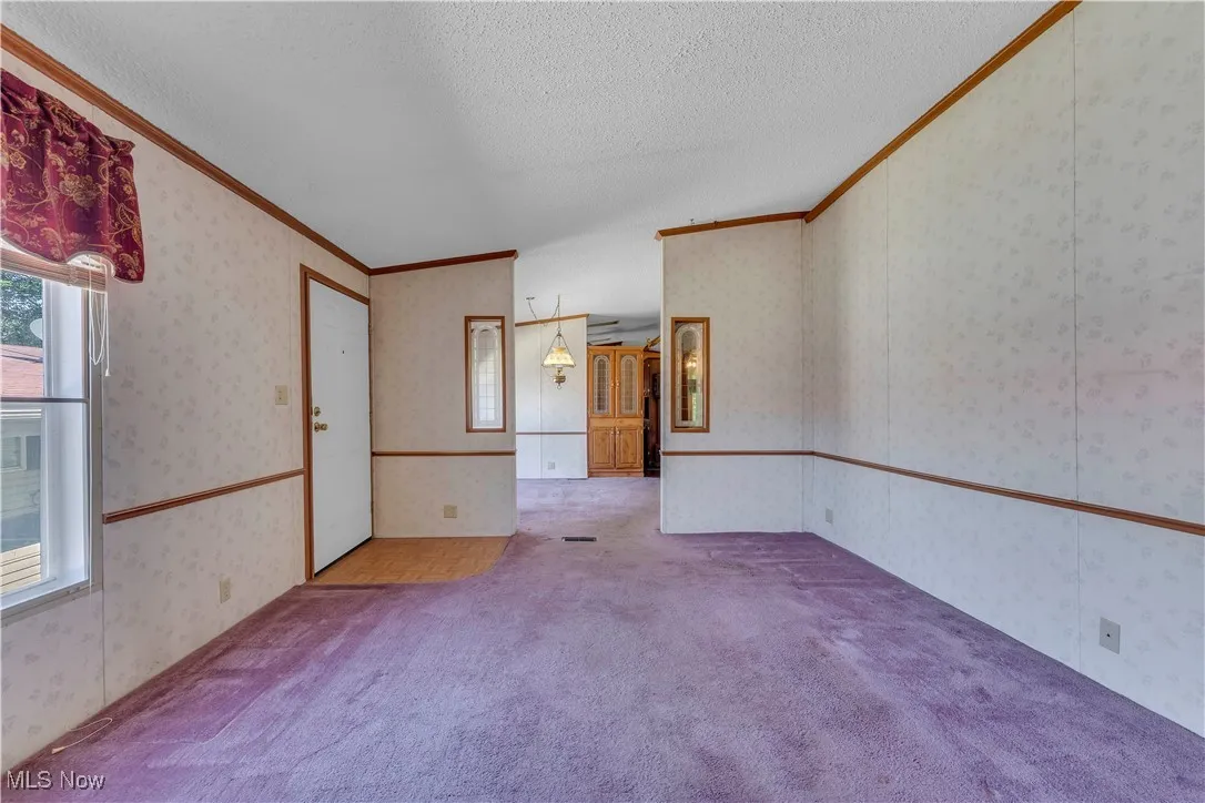 Carpeted empty room with crown molding, wallpapered walls, and a textured ceiling