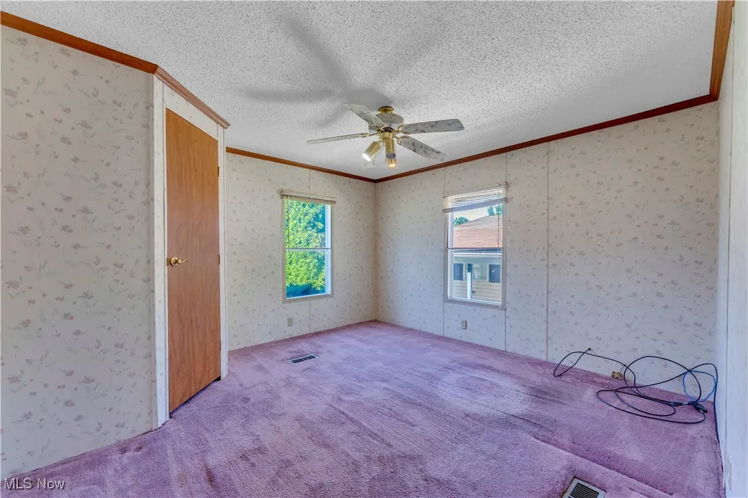 Unfurnished bedroom featuring crown molding, a textured ceiling, carpet, ceiling fan, and wallpapered walls