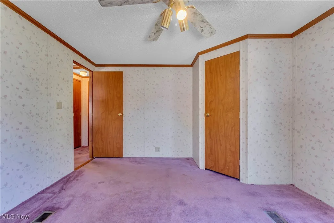 Unfurnished bedroom with crown molding, a textured ceiling, carpet flooring, ceiling fan, and wallpapered walls