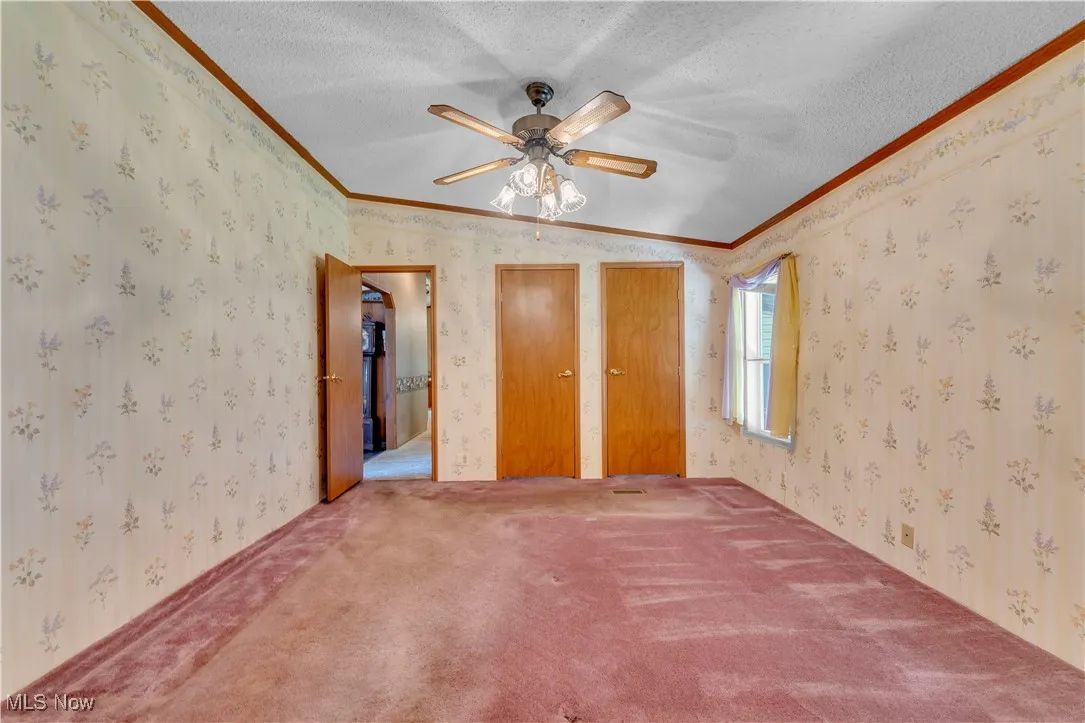 Unfurnished bedroom with wallpapered walls, crown molding, carpet, a textured ceiling, and ceiling fan