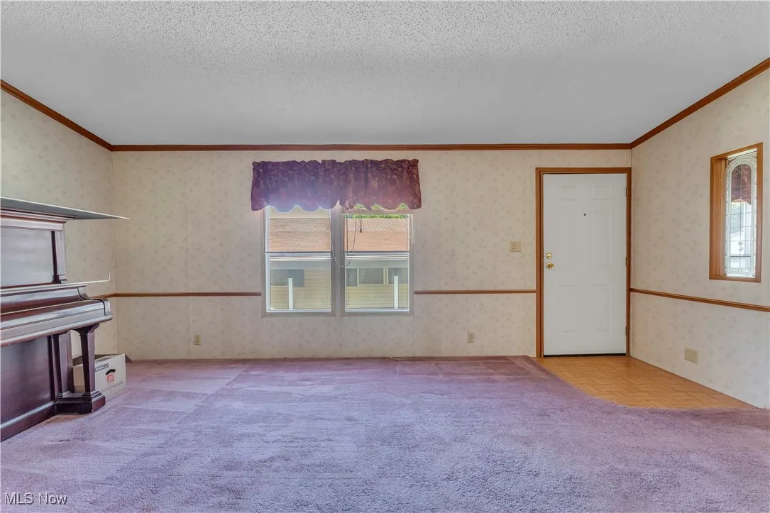 Unfurnished living room with wallpapered walls, ornamental molding, a textured ceiling, and light carpet