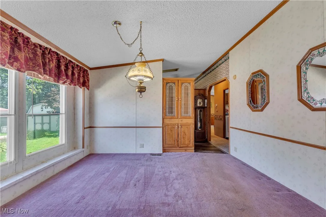 Unfurnished dining area featuring wallpapered walls, crown molding, carpet floors, and a textured ceiling