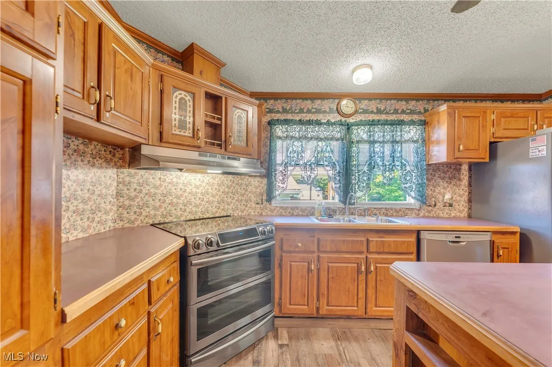 Kitchen with stainless steel appliances, backsplash, light wood-type flooring, light countertops, and a textured ceiling
