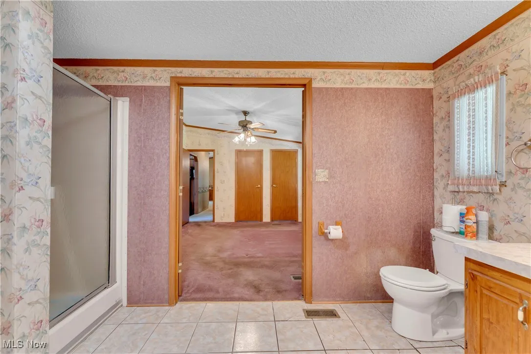 Bathroom featuring vanity, a shower stall, light tile patterned flooring, wallpapered walls, and a textured ceiling