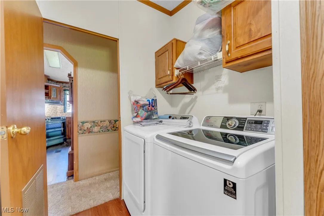Laundry area with cabinet space, light wood-style flooring, washer and dryer, crown molding, and arched walkways