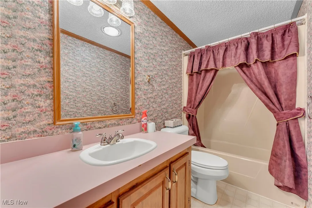 Full bathroom with a textured ceiling, shower / bath combination with curtain, vanity, wallpapered walls, and crown molding