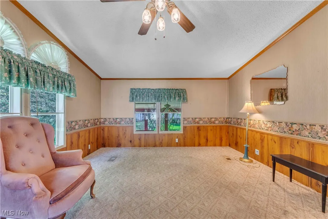 Sitting room with wainscoting, wood walls, ornamental molding, ceiling fan, and carpet