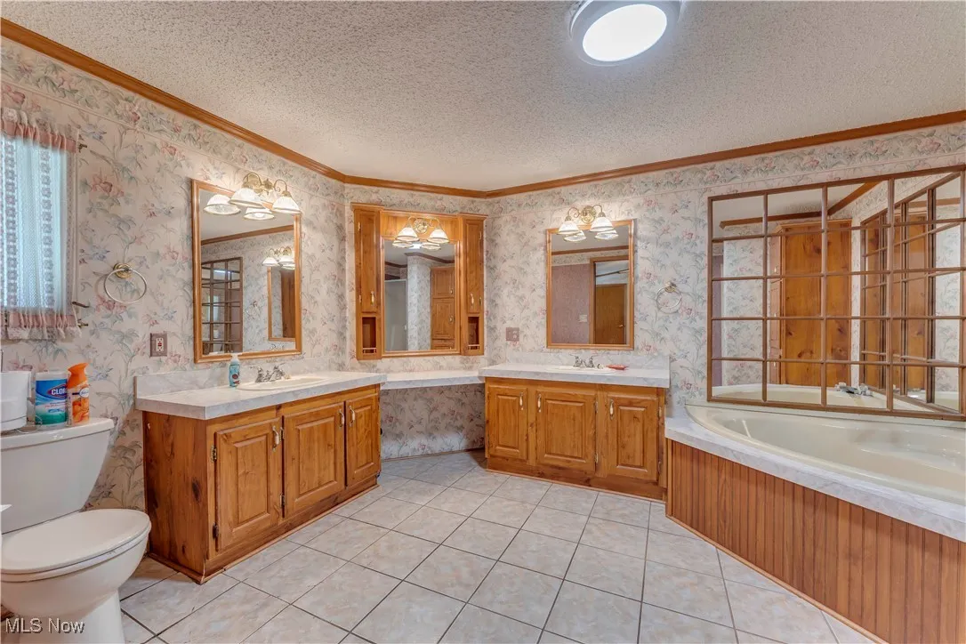 Bathroom with a bath, ornamental molding, two vanities, a textured ceiling, and light tile patterned flooring