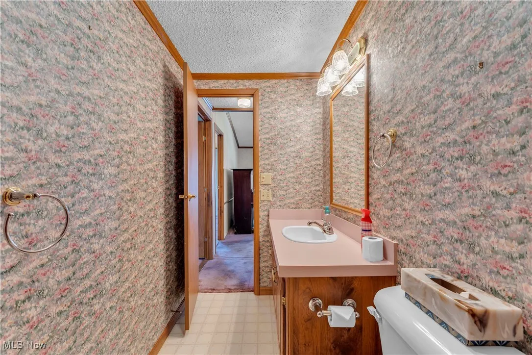 Bathroom featuring vanity, crown molding, wallpapered walls, a textured ceiling, and light flooring
