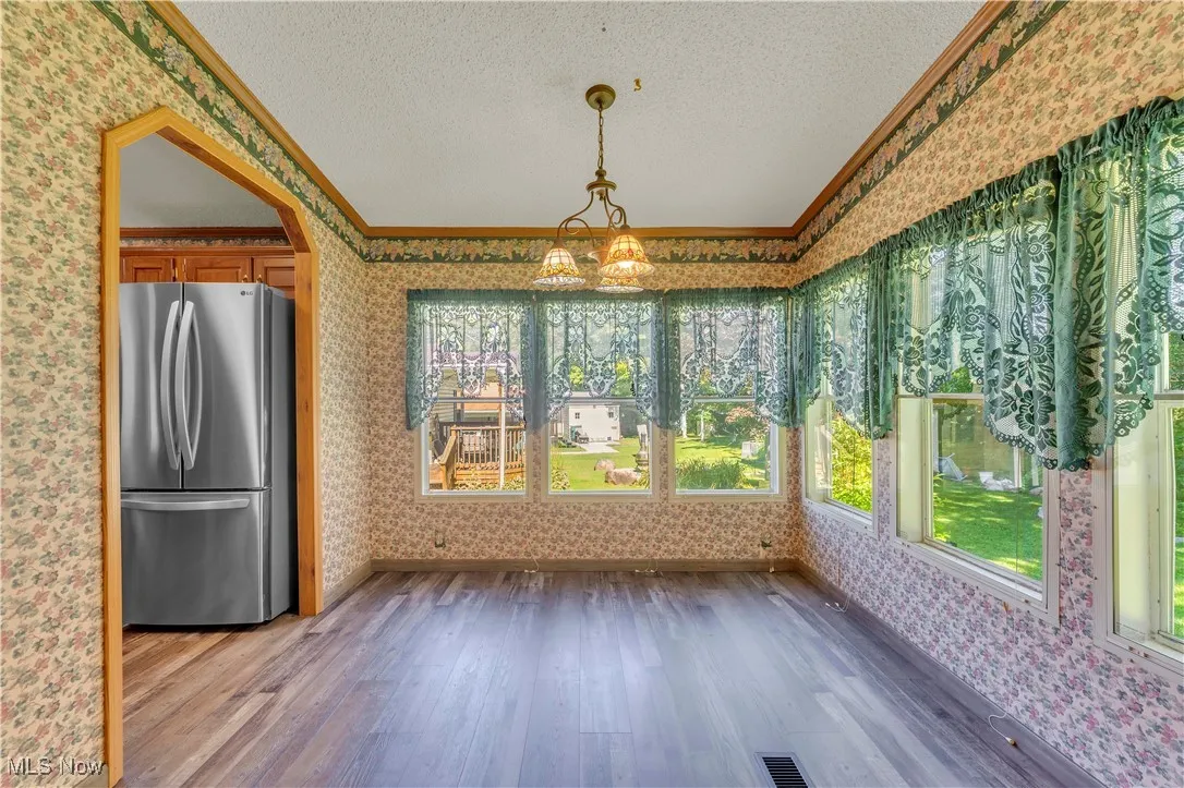 Unfurnished dining area with wallpapered walls, wood finished floors, a textured ceiling, crown molding, and a chandelier