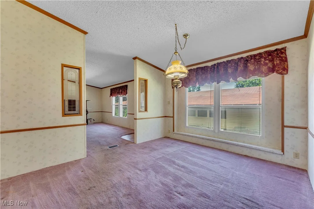 Unfurnished dining area featuring wallpapered walls, ornamental molding, a textured ceiling, carpet, and vaulted ceiling