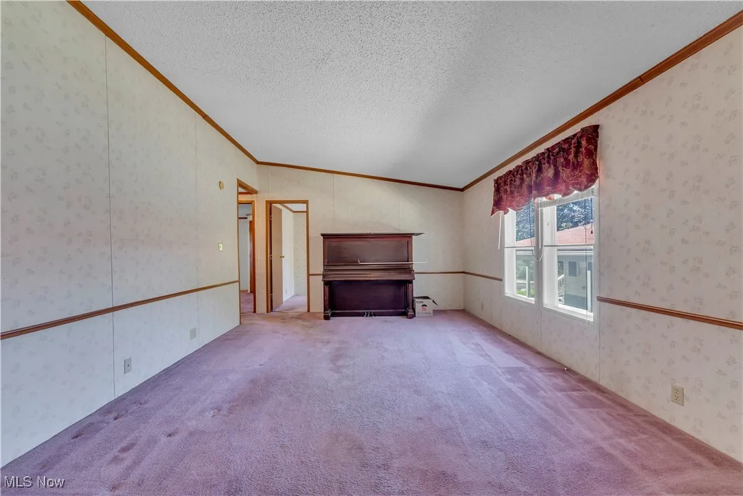 Unfurnished living room featuring crown molding, wallpapered walls, carpet flooring, and a textured ceiling