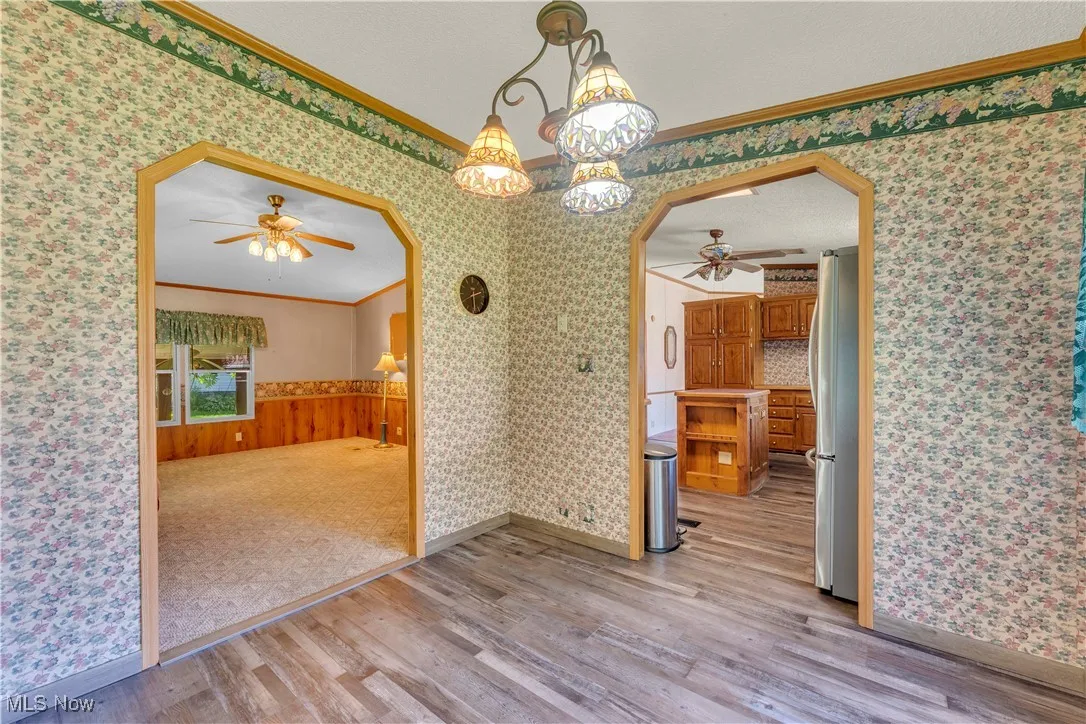 Unfurnished dining area with crown molding, a ceiling fan, wallpapered walls, light wood-style flooring, and arched walkways