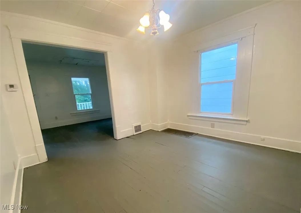 Unfurnished dining area with a chandelier, dark wood-type flooring, and ornamental molding