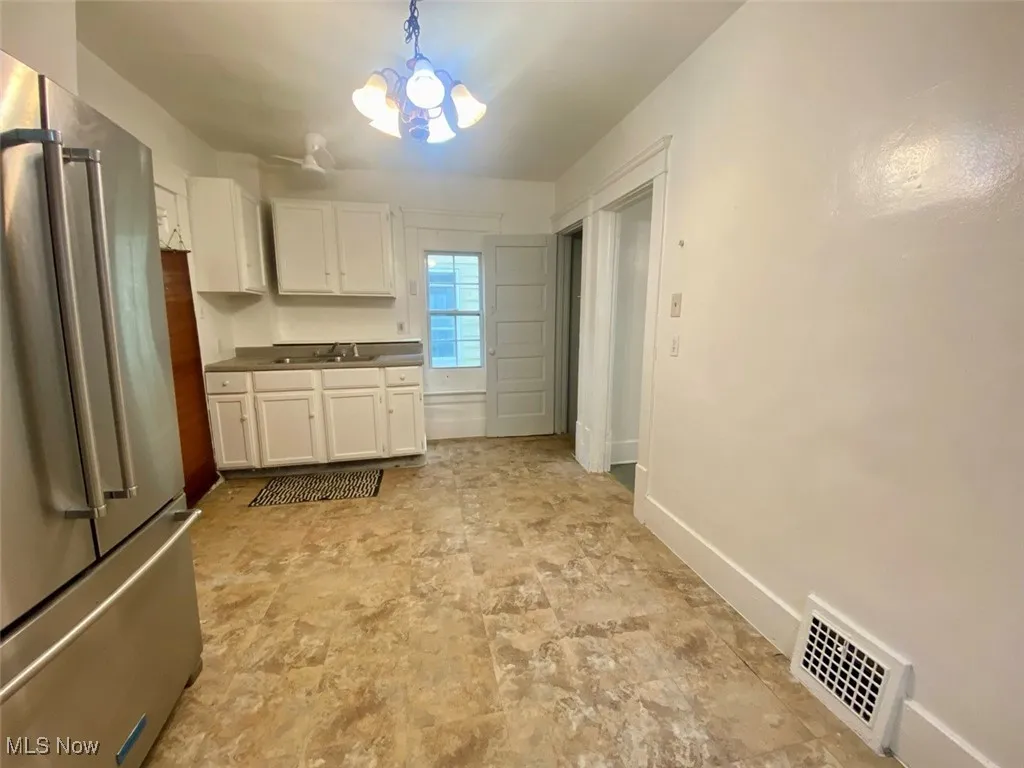 Kitchen featuring freestanding refrigerator, a chandelier, white cabinetry, and decorative light fixtures
