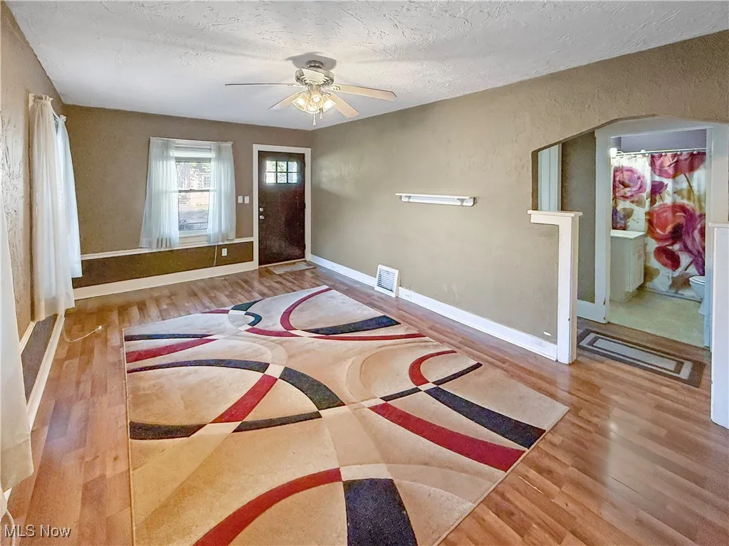 Foyer entrance with wood finished floors, a ceiling fan, a textured ceiling, a textured wall, and arched walkways