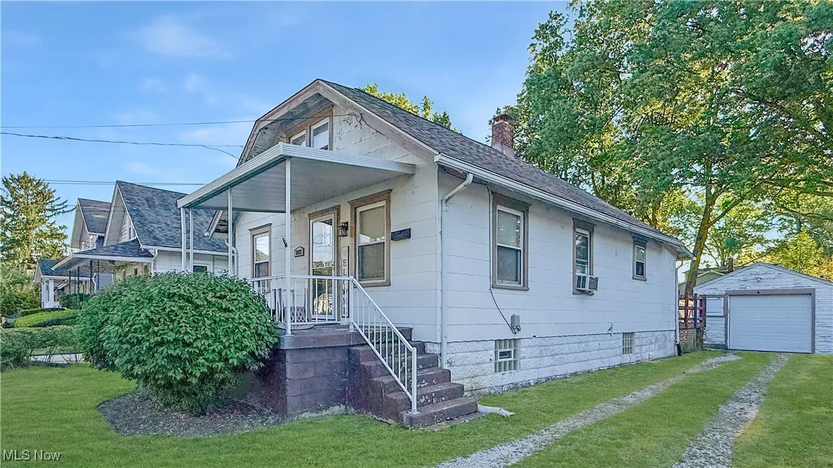 Bungalow-style home with driveway, a detached garage, a chimney, a shingled roof, and a front yard
