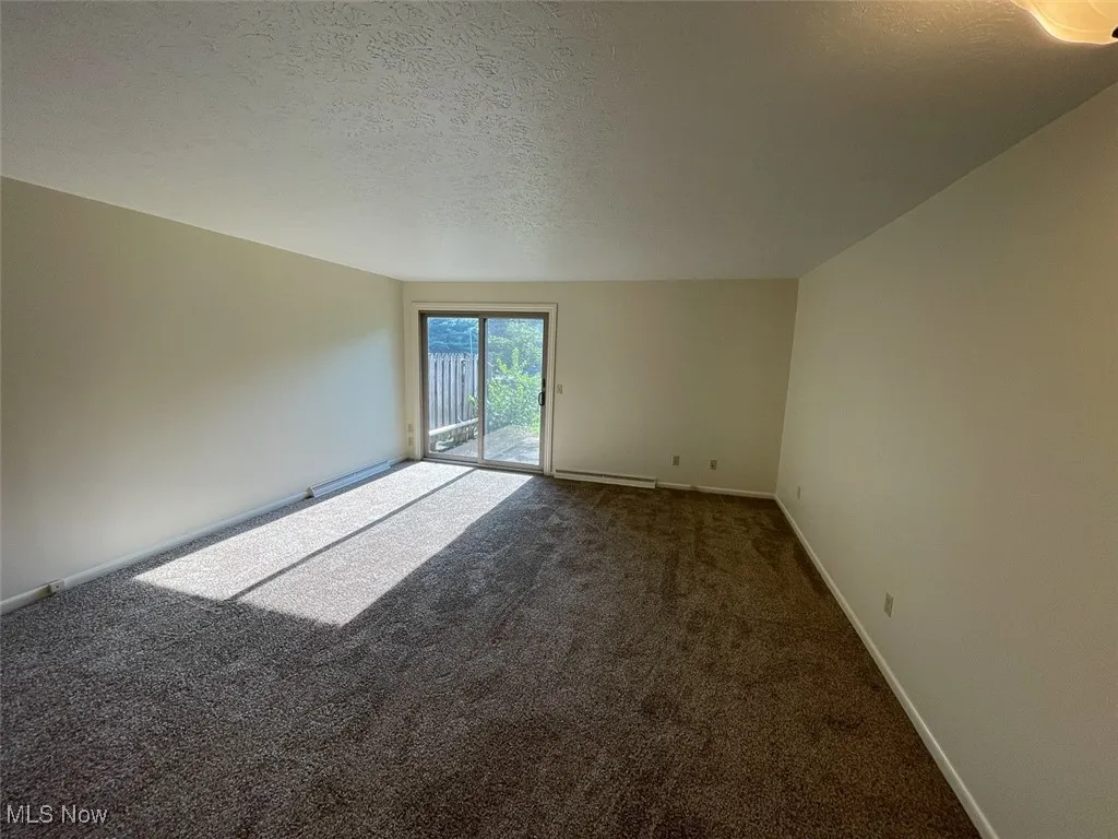 Spare room with a textured ceiling, carpet floors, and a baseboard heating unit