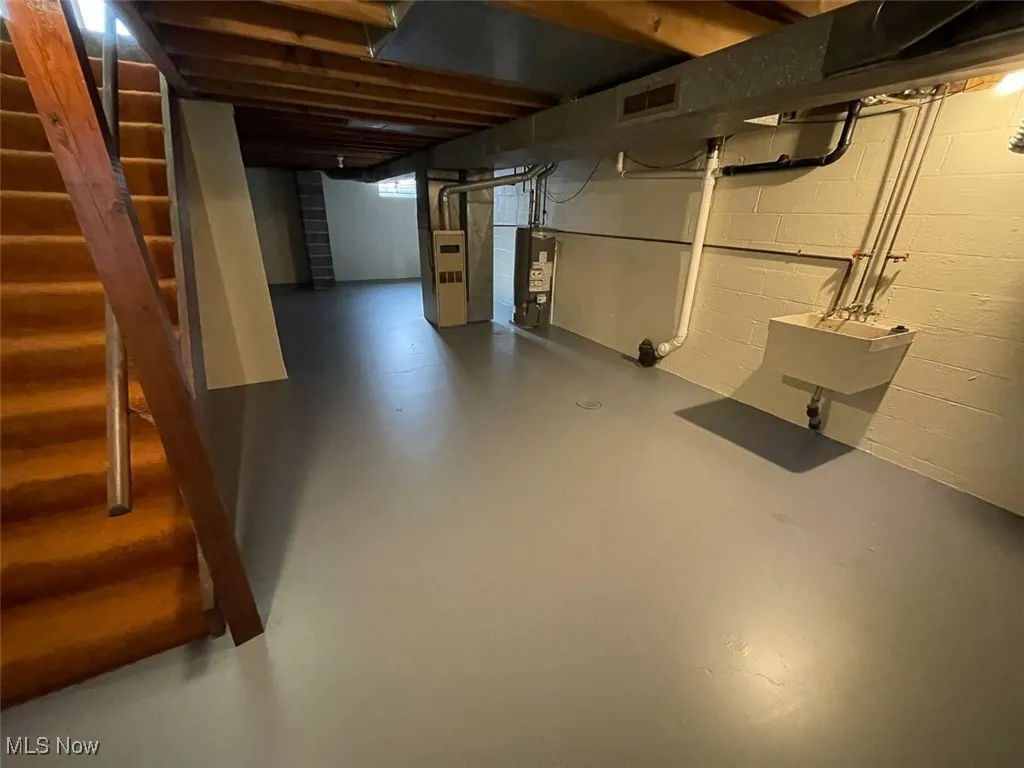 Unfinished below grade area featuring stairway, water heater, and heating unit