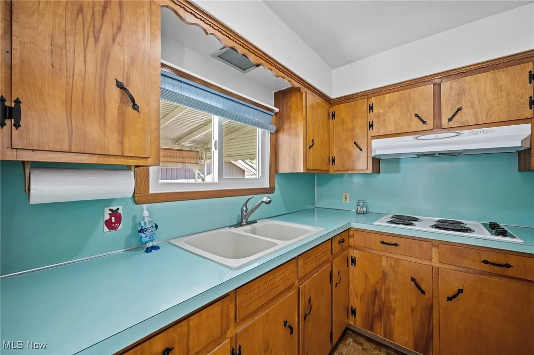 Kitchen featuring brown cabinetry, light countertops, under cabinet range hood, and white electric stovetop