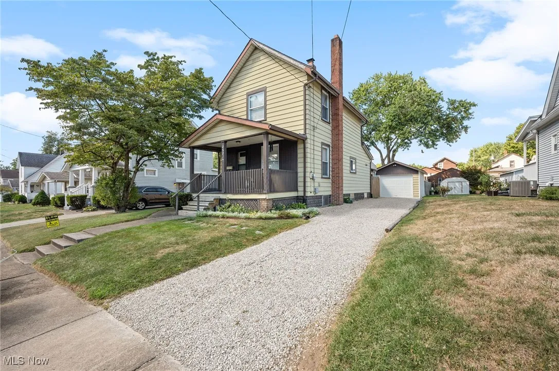 View of front facade with an outdoor structure, covered porch, a chimney, a front lawn, and a detached garage