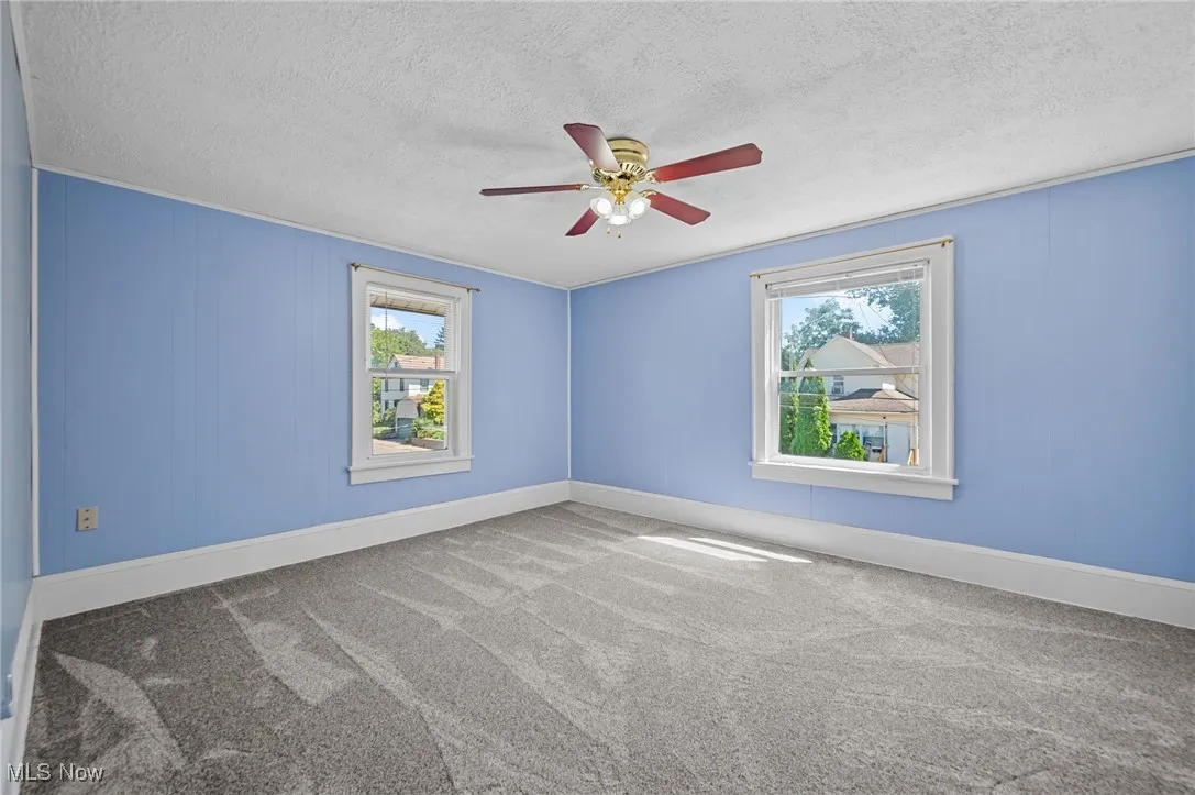 Carpeted empty room with plenty of natural light, a textured ceiling, and ceiling fan