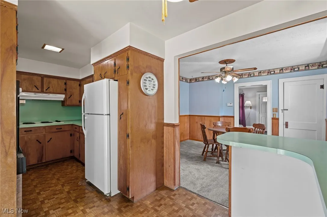 Kitchen featuring freestanding refrigerator, a ceiling fan, wooden walls, light countertops, and wainscoting