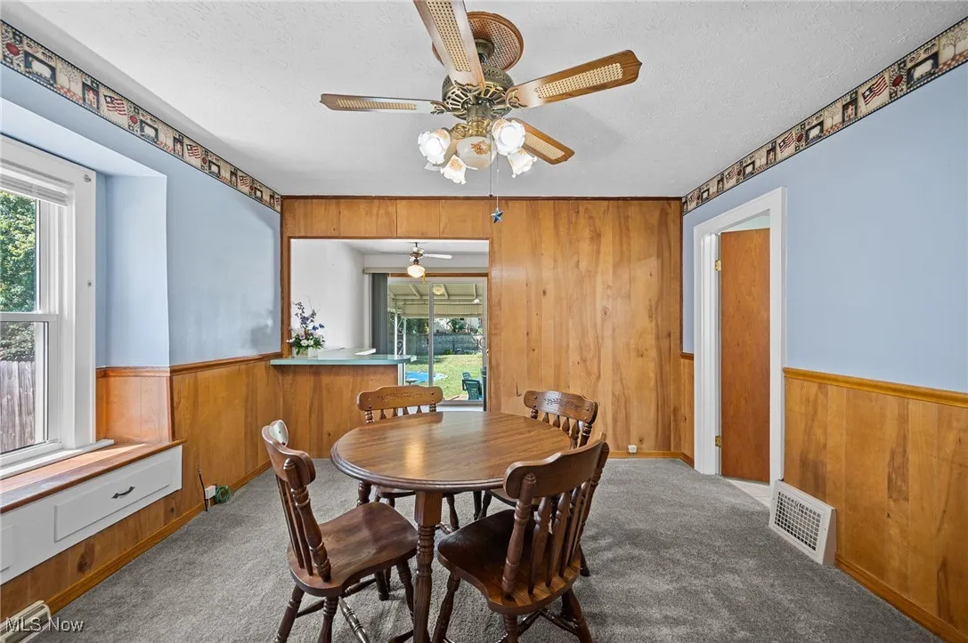 Dining area with wood walls, wainscoting, a textured ceiling, carpet floors, and ceiling fan
