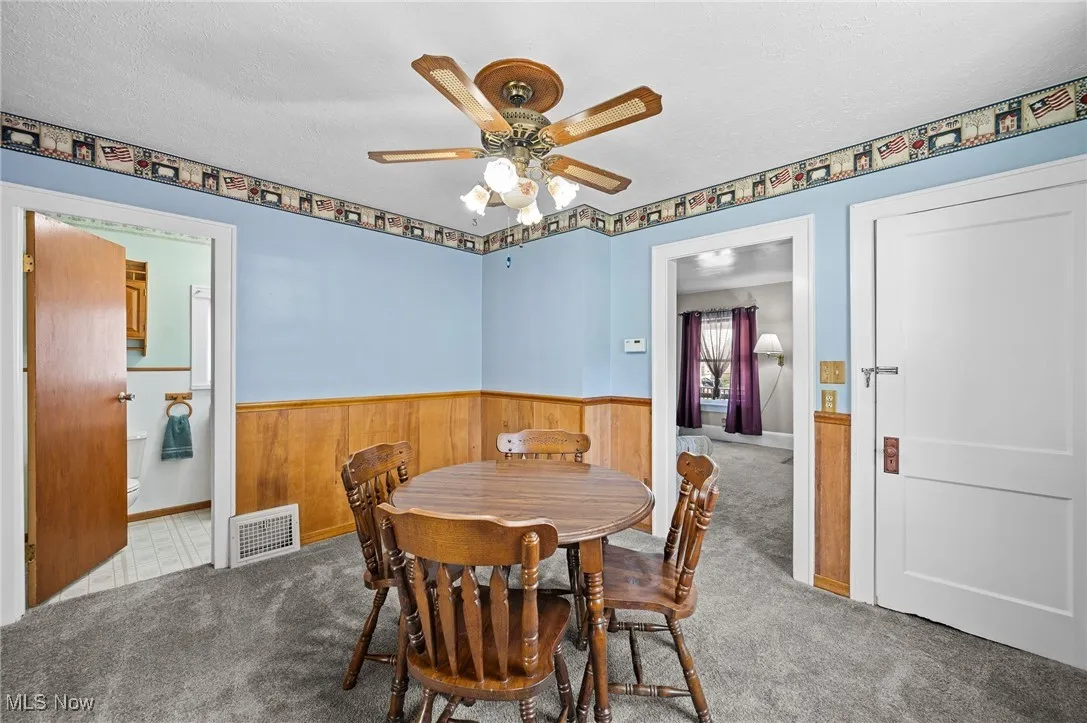 Dining area featuring carpet flooring, ceiling fan, a textured ceiling, wooden walls, and wainscoting