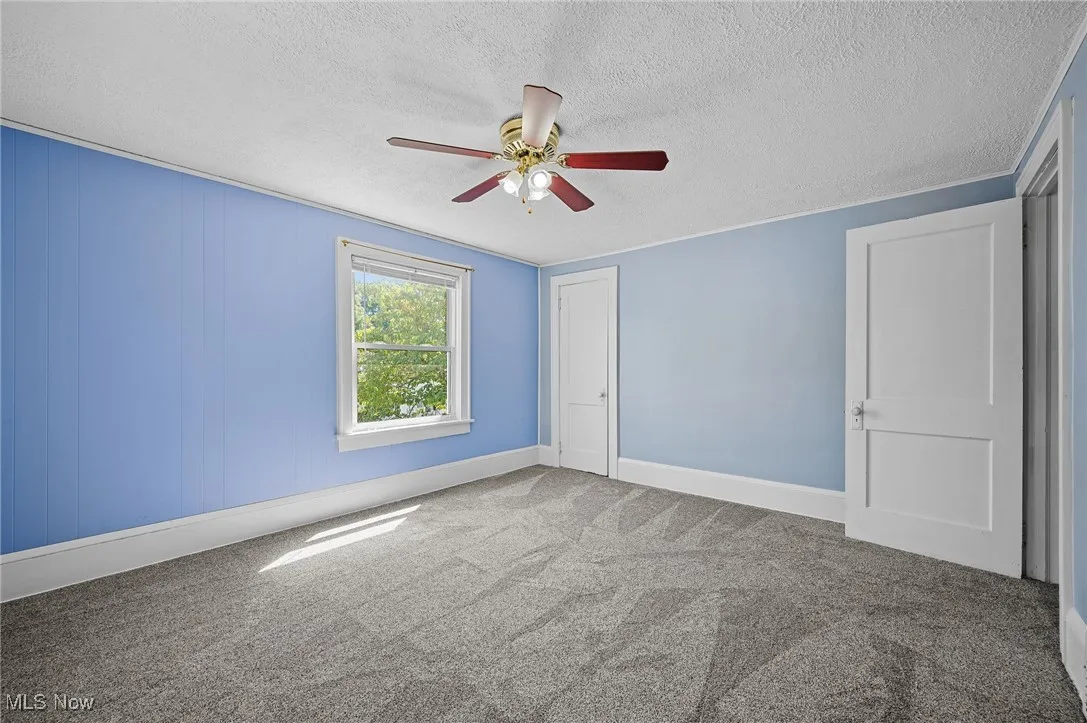 Carpeted empty room with a textured ceiling and a ceiling fan