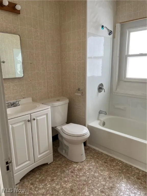 Bathroom with tile walls, bathing tub / shower combination, and vanity