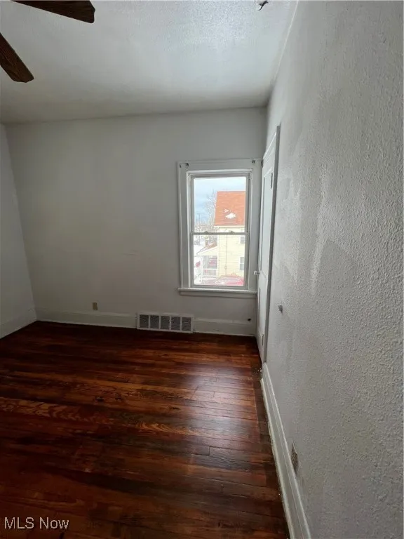 Spare room with dark wood-style flooring, a textured wall, a textured ceiling, and ceiling fan