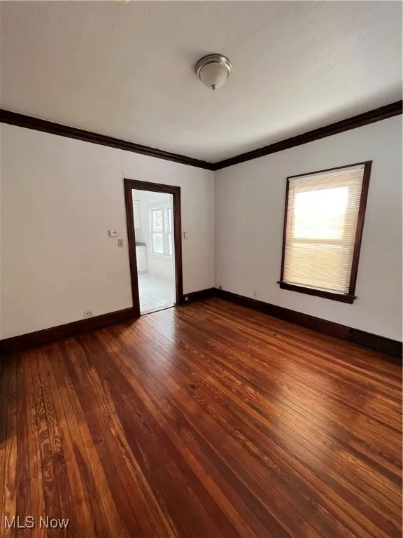 Empty room with ornamental molding, dark wood-style floors, and a textured ceiling