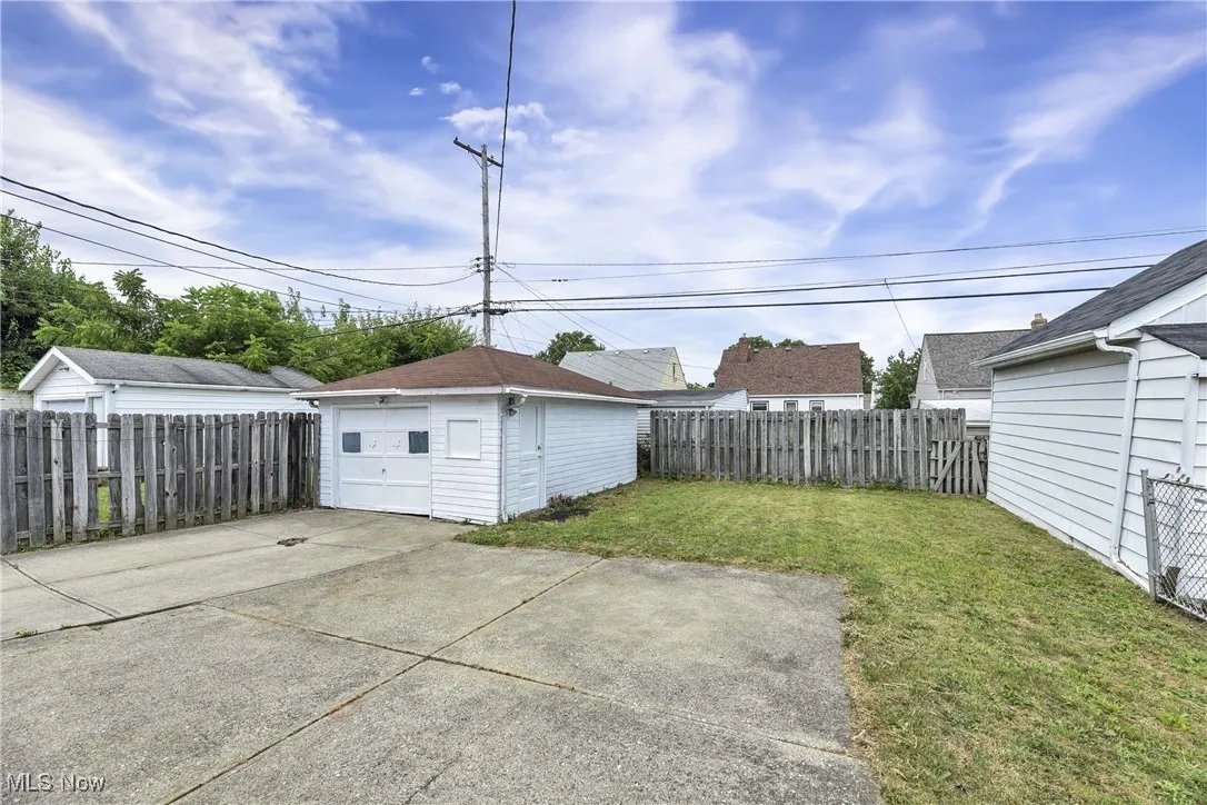 Fenced backyard with an outdoor structure, concrete driveway, and a detached garage