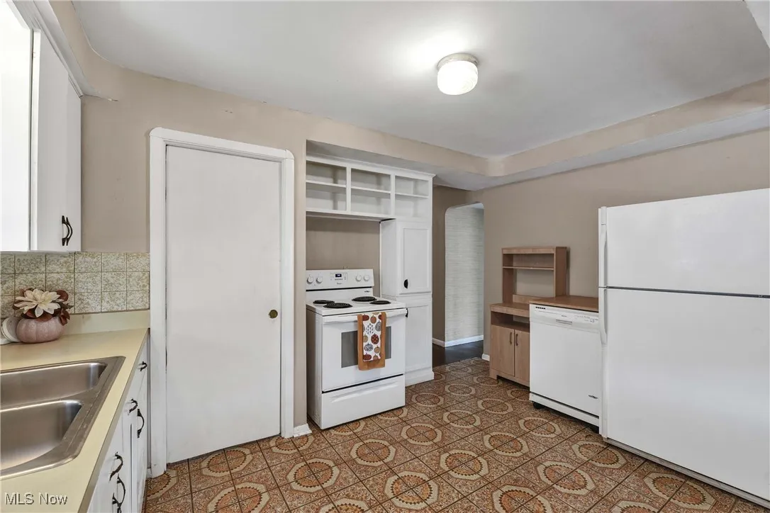 Kitchen featuring white cabinetry, white appliances, arched walkways, light countertops, and open shelves