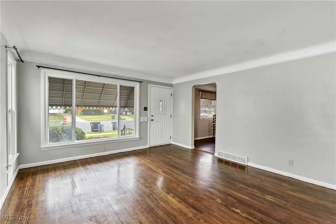Empty room featuring arched walkways, dark wood-type flooring, and crown molding