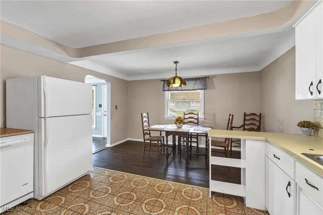 Kitchen with white cabinetry, white dishwasher, light countertops, arched walkways, and decorative light fixtures