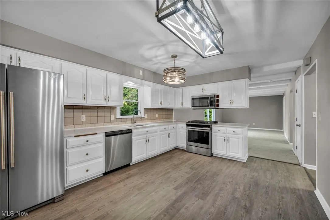 Kitchen featuring stainless steel appliances, white cabinets, light countertops, backsplash, and pendant lighting