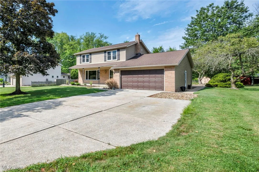 Traditional-style house featuring a front lawn, an attached garage, a chimney, brick siding, and concrete driveway
