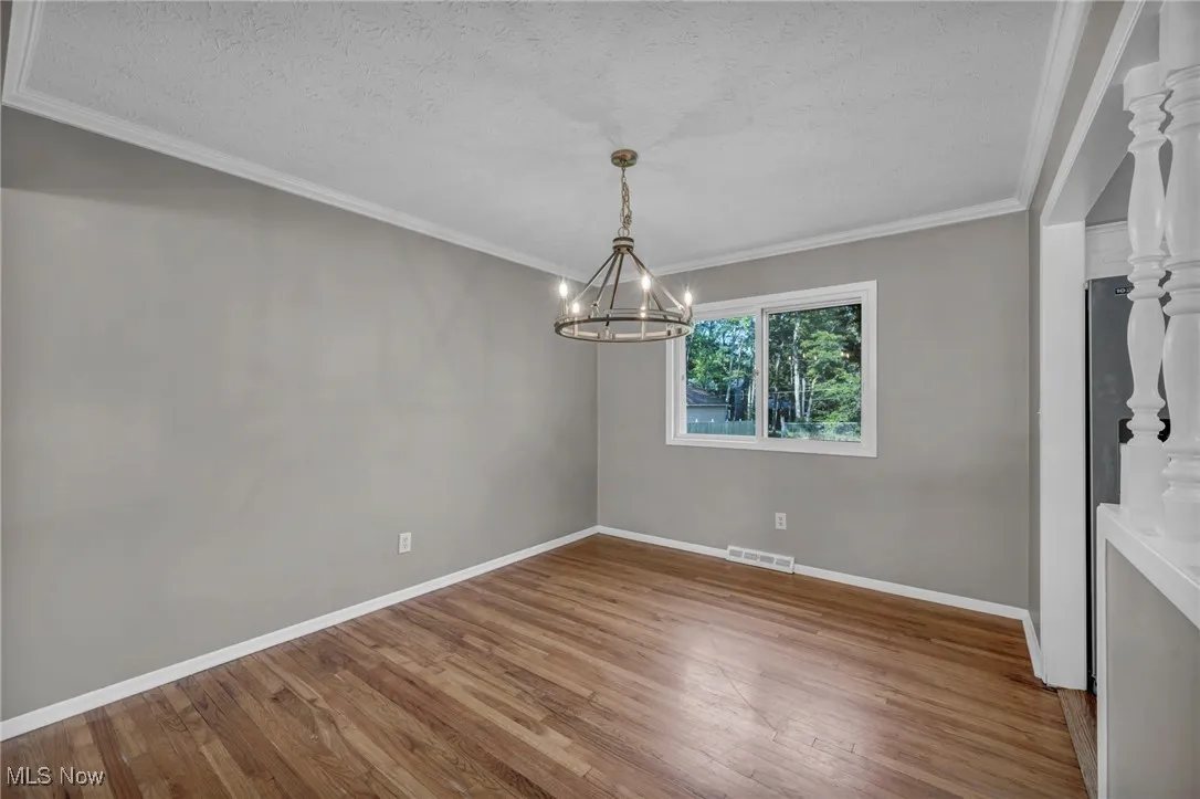 Unfurnished dining area featuring crown molding, wood finished floors, a textured ceiling, and a chandelier