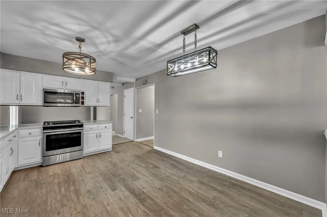 Kitchen featuring white cabinets, stainless steel appliances, light countertops, light wood-type flooring, and pendant lighting