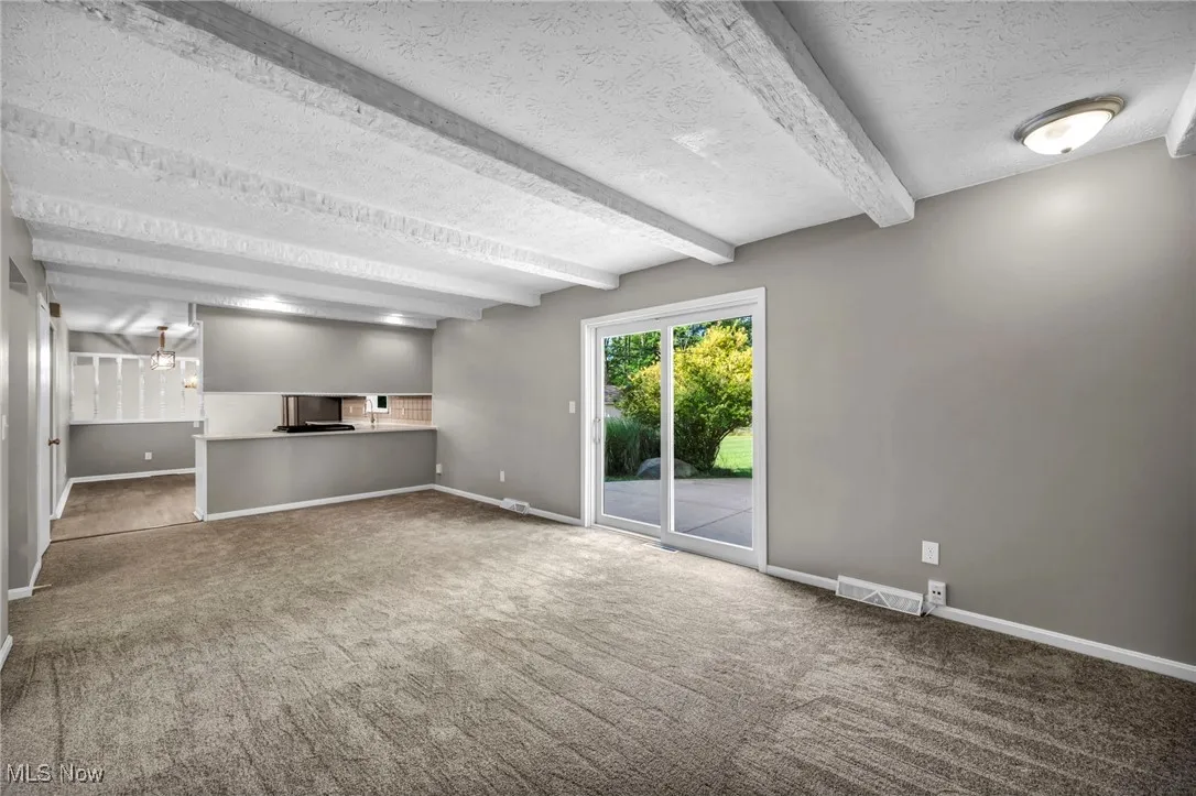 Unfurnished living room with beamed ceiling, a textured ceiling, carpet, and a chandelier