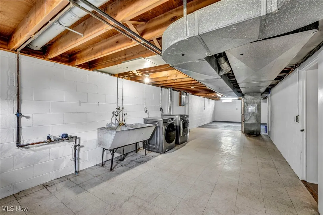 Unfinished below grade area featuring light flooring, washer and clothes dryer, and heating unit