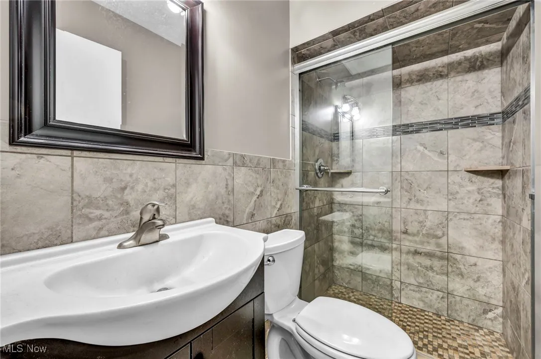 Full bathroom featuring vanity, a stall shower, and tile walls