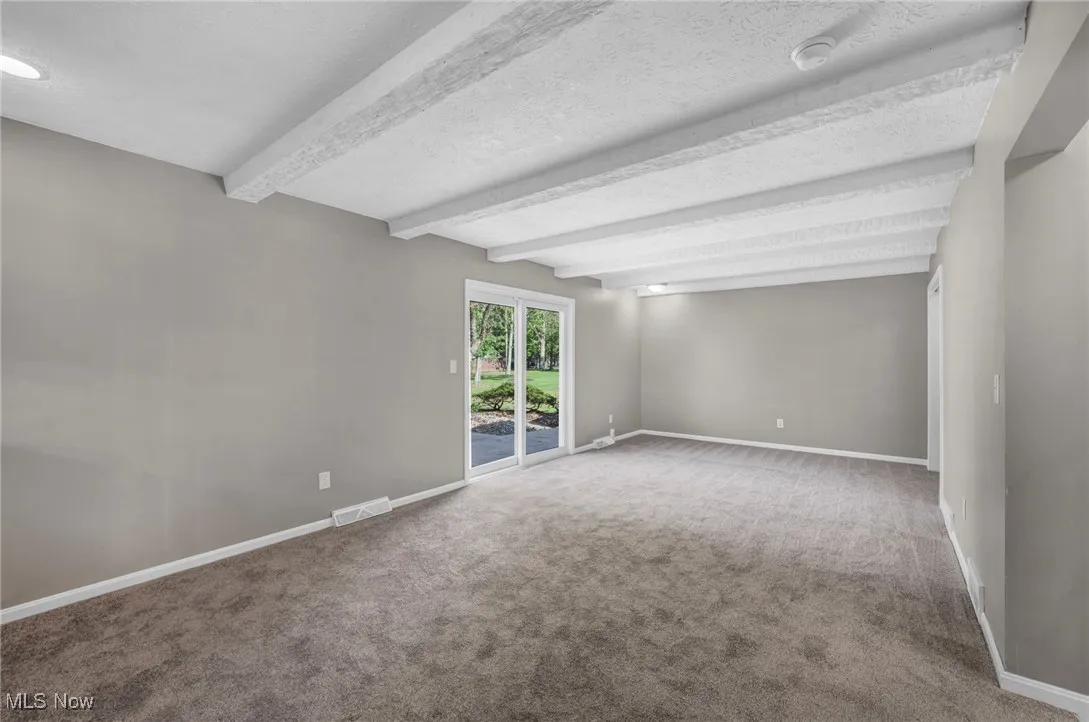 Unfurnished room featuring beam ceiling, a textured ceiling, and carpet flooring
