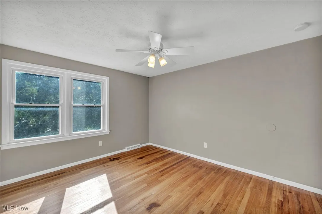 Empty room featuring light wood-style flooring, a textured ceiling, and ceiling fan