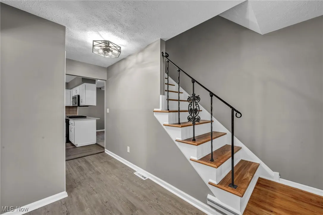 Stairs featuring a textured ceiling, wood finished floors, and a baseboard heating unit
